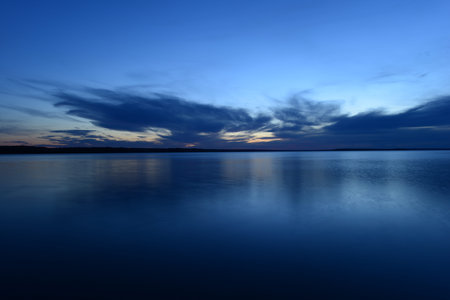 blue sky in the twilight glow from behind clouds over the azure calm surface of the water