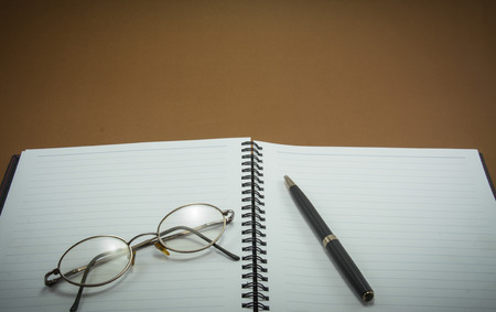 notebook with pen and eye glasses on brown backgroundの写真素材