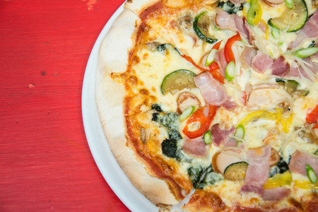 Hot pizza slice with melting cheese on red wooden table.の写真素材
