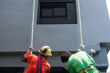 Painters and harnesses hanging high building at construction site,hand brush color work conceptの写真素材