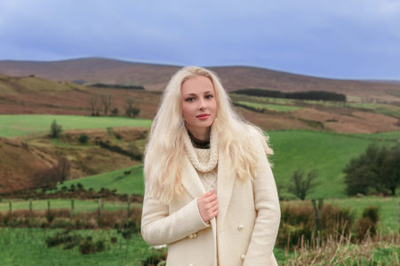Beautiful young caucasian blonde woman in a white jumper standing in the field overlooking...