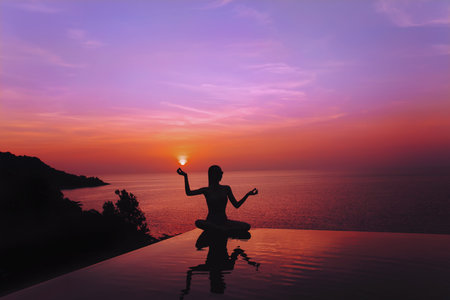 A silhouette of a girl sitting on the edge of the swimming pool overlooking amazingly beautiful...