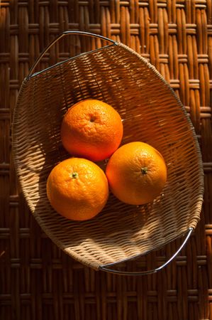 Three oranges in the wattled bowl on the tableの写真素材