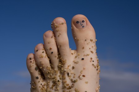 closeup of a man's foot with painted face on a toe on little stones on a blue skyの写真素材