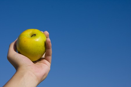 closeup of an apple in girl's hand over blue skyの写真素材
