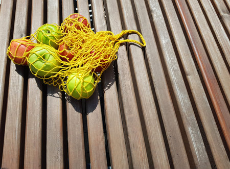 Red and green apples in an eco-friendly yellow bag lie on a bench. minimalist horizontal photo