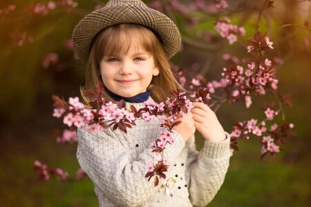 Spring portrait, adorable little girl in hat walk in blossom tree garden on sunsetの写真素材