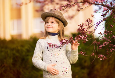 Spring portrait, adorable little girl in hat walk in blossom tree garden on sunsetの写真素材