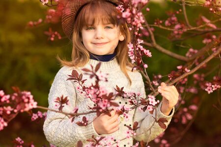 Spring portrait, adorable little girl in hat walk in blossom tree garden on sunsetの写真素材
