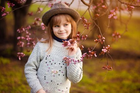 Spring portrait, adorable little girl in hat walk in blossom tree garden on sunsetの写真素材
