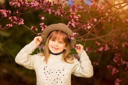 Spring portrait, adorable little girl in hat walk in blossom tree garden on sunsetの写真素材