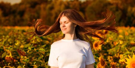 Summer portrait of happy young woman in white with flying hair in sunflower fieldの写真素材