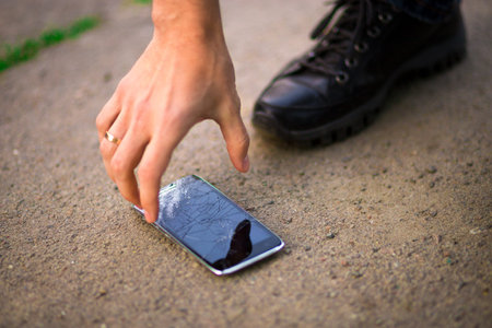 Person Picking Broken Smart Phone Cracked Screen on Ground