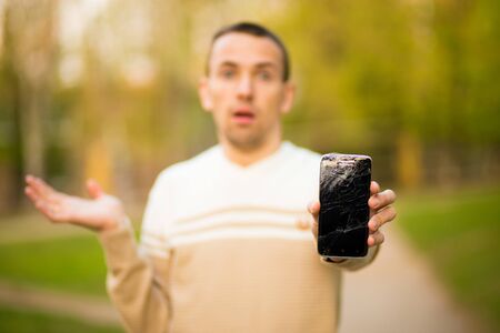 Handsome young man hold broken smartphone screen stressed with hand on head, shocked with shame and surprise face, angry and frustrated. Fear and upset for mistake.の写真素材