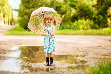 happy child girl with an umbrella and rubber boots in puddle on summer walkの写真素材