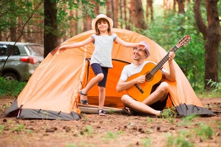 Father and daughter near camping tent playing guitar in summer forestの写真素材