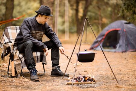 Young man camping in tent on autumn day and cook food on campfire. Vacation Conceptの写真素材