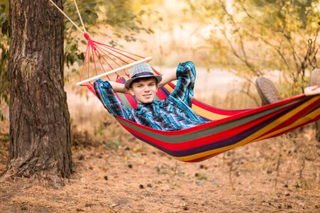 Young happy free man in hat relaxing outside in hammock in autumn forestの写真素材