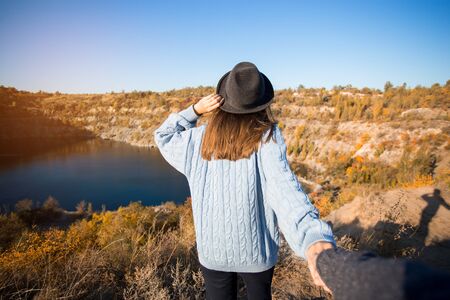 Tourist woman in black hat holding man by hand and go to lake in autumn mountains. Follow me conceptの写真素材