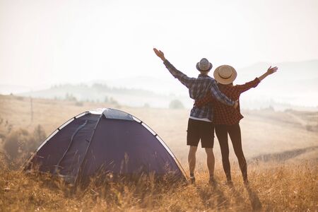 Silhouette of loving couple travel relax camping in autumn holiday. On top of moutain. Enjoy sunrise together with hands up.の写真素材