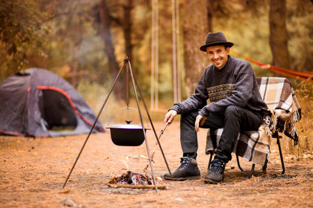 Young man camping in tent on autumn day and cook food on campfire. Vacation Conceptの写真素材