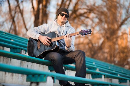 Young man sitting on steps playing guitar and singingの写真素材