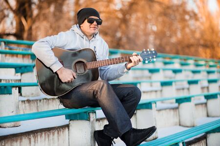 Young man sitting on steps playing guitar and singingの写真素材