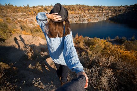 Tourist woman in black hat holding man by hand and go to lake in autumn mountains. Follow me conceptの写真素材
