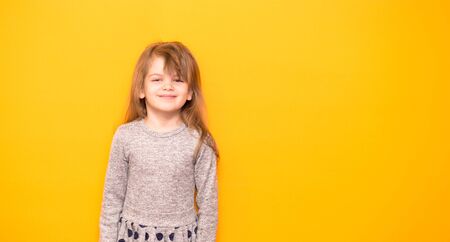 Portrait of cute smiling little girl in grey dress over yellow background.の写真素材