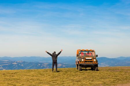 Happy man with hands up travel by car on mountains top. Travel conceptの写真素材