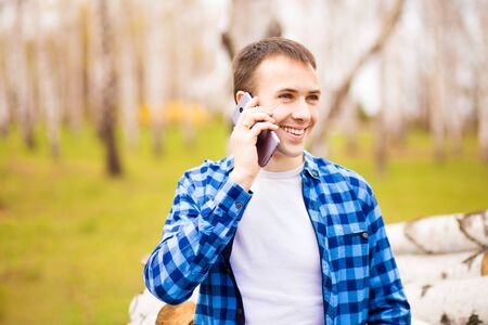 Image of happy young man walking in city park and talking by his phone.の写真素材