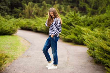 Young girl walks along in white jacket and jeans by summer parkの写真素材