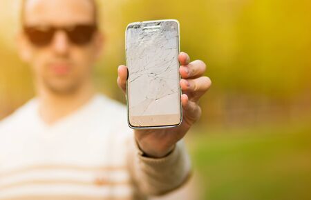 guy holding black smartphone with broken display. Broken screen of modern frameless phone. guy crying with his eyes closedの写真素材