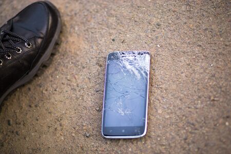 Person Picking Broken Smart Phone Cracked Screen on Groundの写真素材