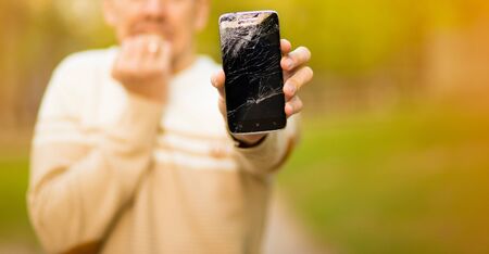 Handsome young man hold broken smartphone screen stressed with hand on head, shocked with shame and surprise face, angry and frustrated. Fear and upset for mistake.の写真素材