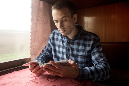 Young man sits at table in train read book. Travel concept