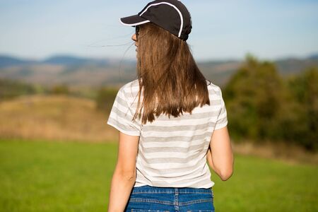 Back view slim young woman in cap enjoy ridge mountains view. Female traveller admire nature in summer vacation. Tourism concept.の写真素材