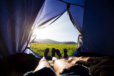 Two people lying in tent, view from inside. Couple camping with beautiful view of mountains sunsetの写真素材