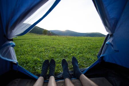 Two people lying in tent, view from inside. Couple camping with beautiful view of mountains sunsetの写真素材