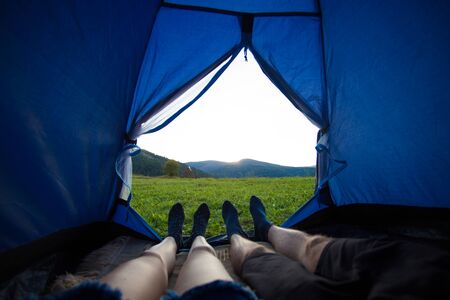 Two people lying in tent, view from inside. Couple camping with beautiful view of mountains sunsetの写真素材