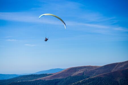 Paraglide silhouette flying over Carpathian peaks mountains on blue sky background. Feeling of freedomの写真素材