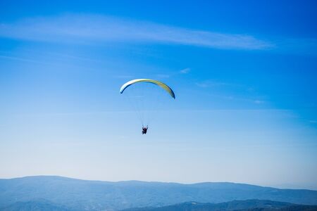 Paraglide silhouette flying over Carpathian peaks mountains on blue sky background. Feeling of freedomの写真素材