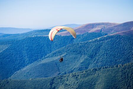 Paraglide silhouette flying over mountain peaks, beautiful rays of light in high mountain valley on backgroundの写真素材