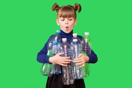 Photo of confused funny little girl holding plastic bottles and looking at camera isolated over green background. ecology conceptの写真素材