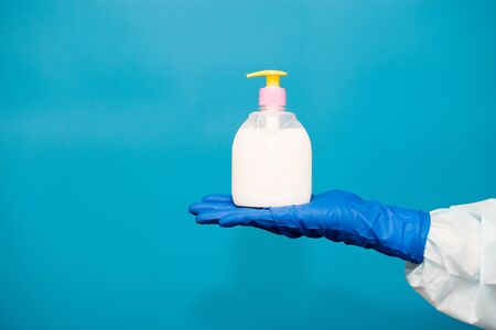 Person hand in blue glove hold soap bottle isolated on blue background. Hands hygiene virus spreading pandemic preventionの写真素材