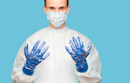 Doctor in medical suit protective mask and gloves washing hands before operating isolated on blue background. Hospital concept. Hands hygiene virus spreading pandemic preventionの写真素材