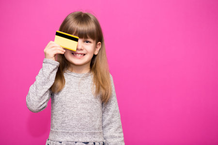 Happy little girl with credit card isolated on pink background.