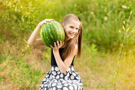 Outdoor portait of happy smilling little girl with watermelon on grass in summertimeの写真素材