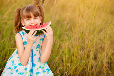 Happy cute little girl eating watermelon on grass in summertimeの写真素材