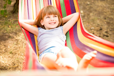 Happy lovely child girl relaxing in colorful hammock in summer forest. Summer vacationの写真素材